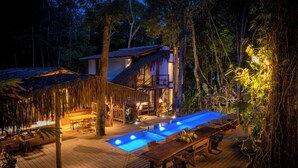 A thatched-roof structure with a pool and wooden deck, surrounded by dense forest. - Vila Morena Altos de Itapororoca (Porto Seguro)