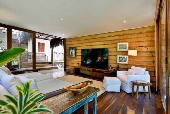 Amplia sala de estar con una gran televisión de pantalla plana, sofás blancos y una mesa de centro de madera.