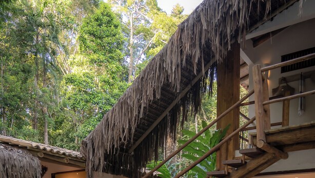 A pool area with a wooden staircase leading to a building with a thatched roof. - Vila Morena Altos de Itapororoca (Porto Seguro)