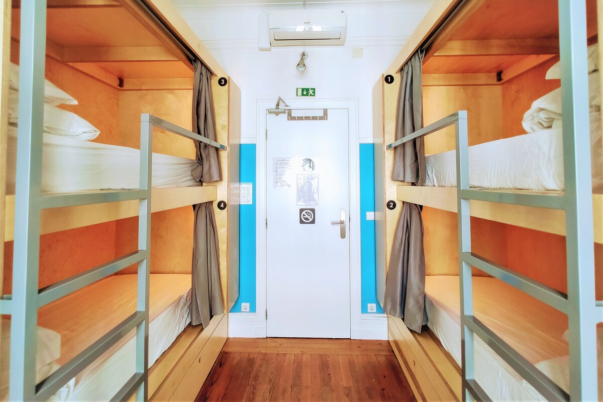 A corridor with bunk beds, a door with a green exit sign, and an air conditioning unit.