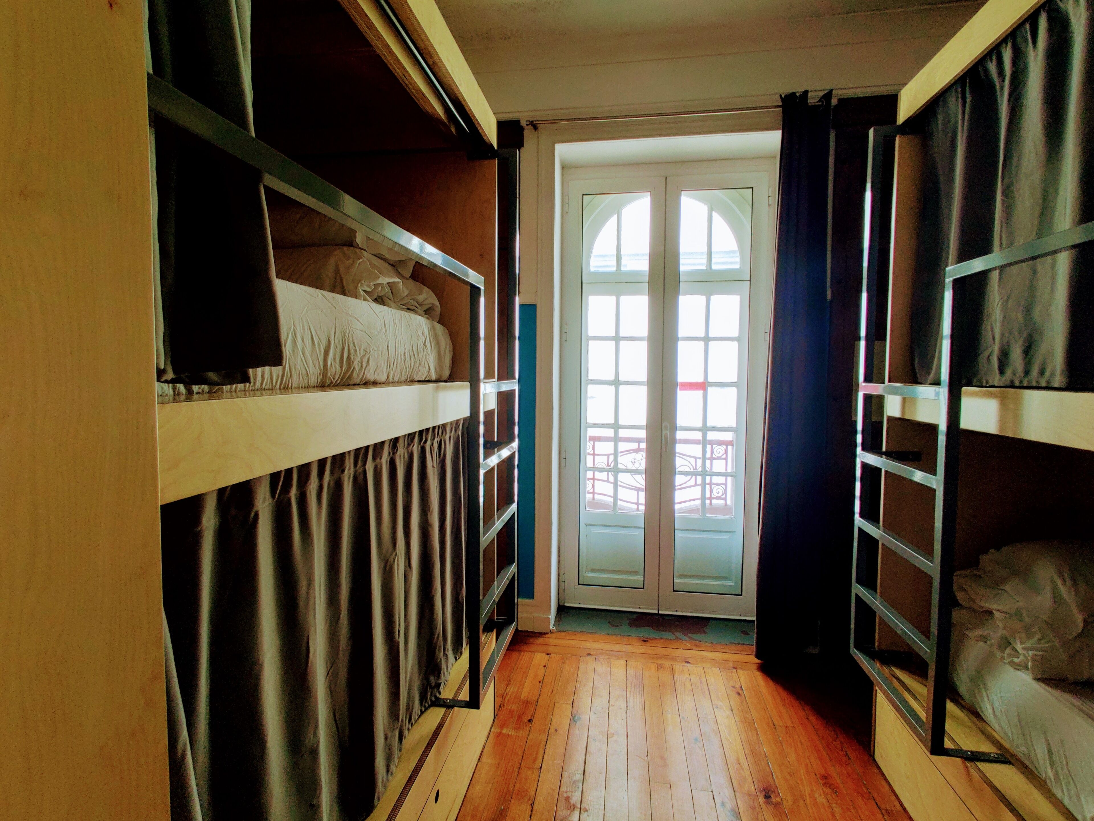 A narrow room with bunk beds, a wooden floor, and a sliding glass door leading to a balcony.