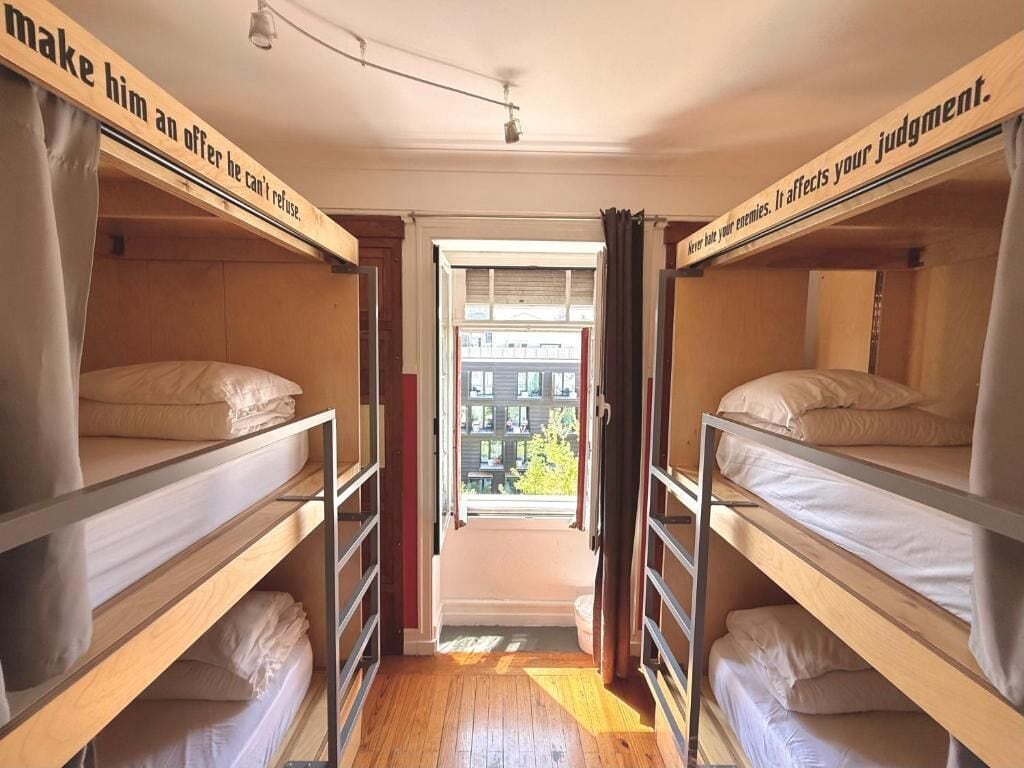 A room with bunk beds, a window with curtains, and a view of buildings outside.