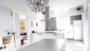 A modern kitchen with white cabinets, a central island, and a hanging light fixture. - Rivoli Cinema Hostel (Porto)