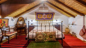 A room with a sloped ceiling, a bed with a metal frame, a wooden chair, a red and black striped rug, and a large vase with a plant. - Eros Home, Panoramic Sea View, Perfect location (Pylos-Nestoras)