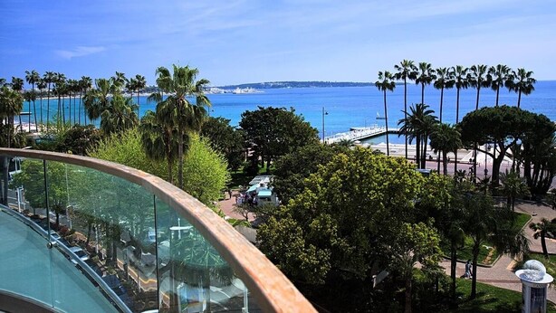 Un hôtel situé sur la côte, offrant une vue sur la mer, des palmiers et une promenade en bord de mer.