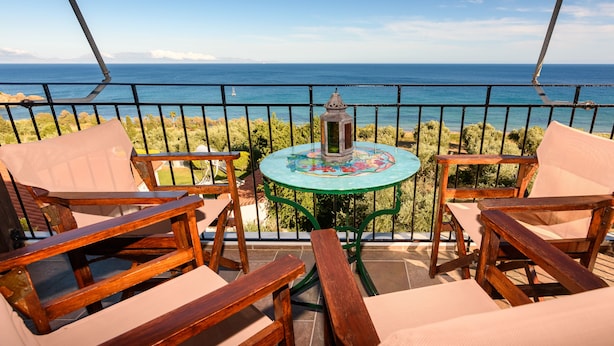 Un balcón con mobiliario de madera y una mesa, con vistas a un paisaje marino.
