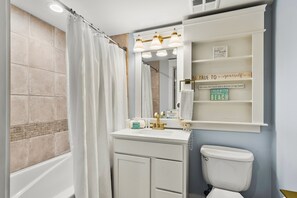 A bathroom with a bathtub, a toilet, a sink, and a vanity with shelves.
