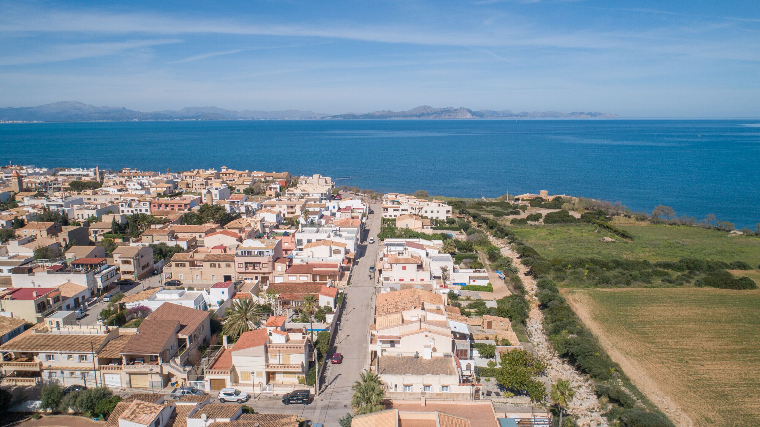Une ville côtière où se côtoient des immeubles résidentiels et des espaces ouverts, offrant une vue dégagée sur la mer et les montagnes lointaines.