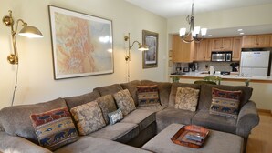 A living room with a sectional sofa, a coffee table, and a kitchen in the background.