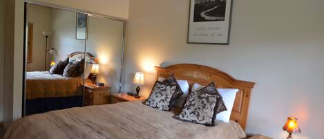 A neatly made bed with a beige comforter and patterned pillows, a wooden headboard, bedside lamps, a mirror, and a framed picture on the wall.