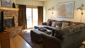 A living room with a stone fireplace, a sofa set, and a large window with curtains.