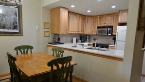 A kitchen with wooden cabinets, a microwave, a refrigerator, a sink, and a dining table with chairs.