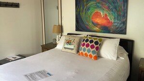 Une chambre d’hôtel avec un grand lit, une table de chevet avec une lampe, un miroir et un tableau abstrait aux couleurs vives accroché au mur.