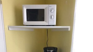Une petite cuisine équipée comprenant un micro-ondes posé sur une étagère, une machine à café et un petit réfrigérateur.