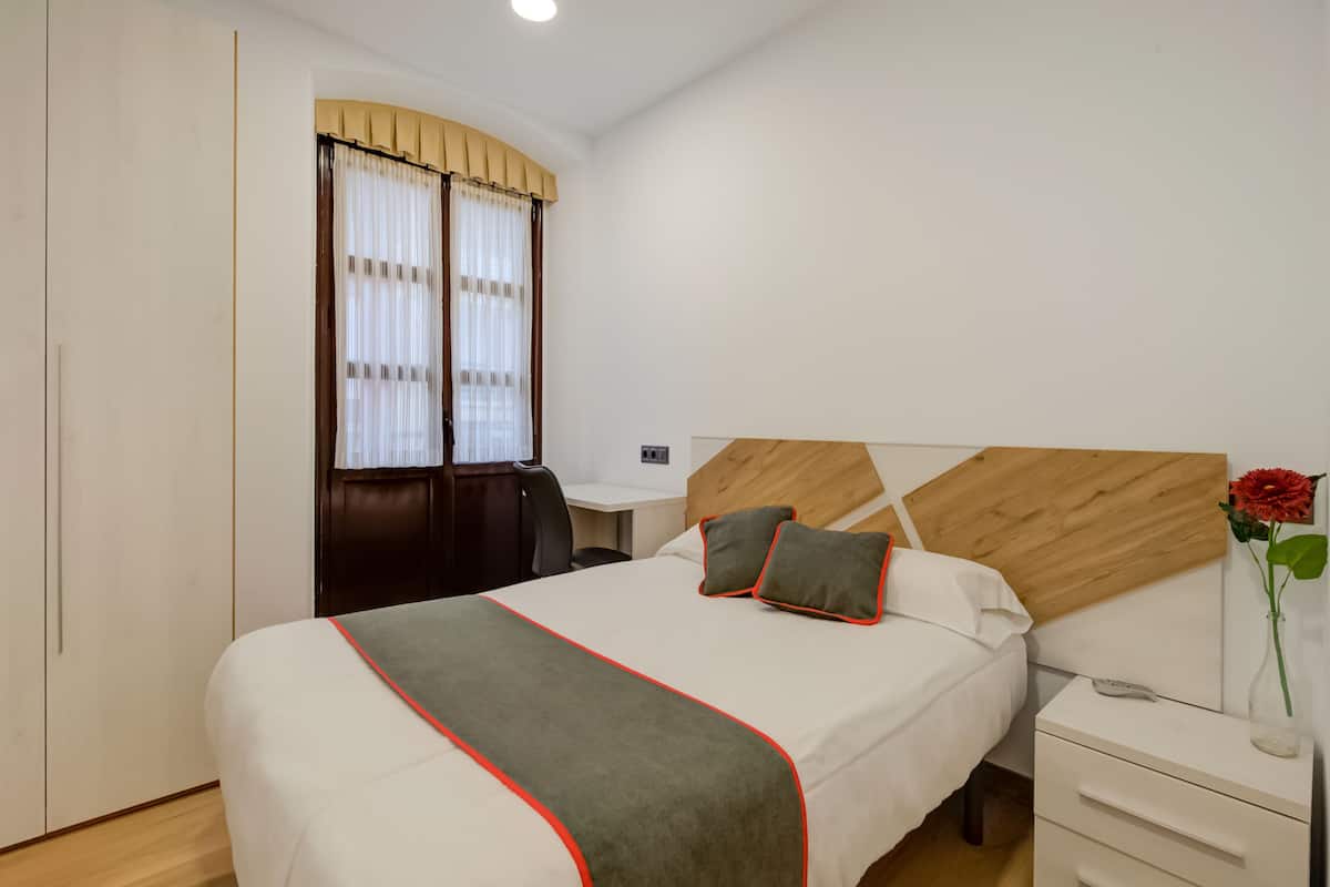 Una habitació d'hotel amb un llit, una taula de nit i un escriptori amb una cadira.