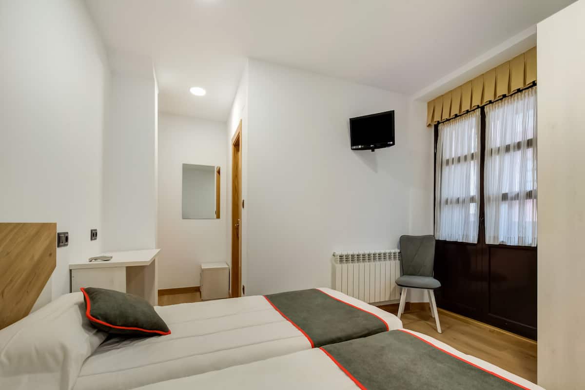 Habitació d'hotel amb un llit, escriptori, cadira, televisió i finestra amb cortines.