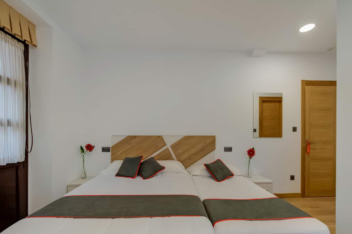 Habitació d'hotel moderna amb un llit gran, dues taules de nit, un panell de capçalera de fusta, una porta de fusta i una finestra amb cortines.