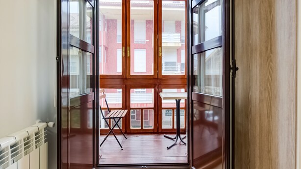 A view through a glass door into a balcony with a wooden table and chair. - OYO Hotel Restaurante La Pinta (Ampuero)