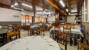 A restaurant with multiple round tables, wooden chairs, and overhead fluorescent lighting. - OYO Hotel Restaurante La Pinta (Ampuero)