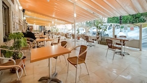 An outdoor cafe with tables and chairs, potted plants, and a view of parked cars. - OYO Hotel Restaurante La Pinta (Ampuero)