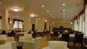 A spacious hotel lobby with multiple dining tables and chairs, a reception area, and a large window providing natural light. - Grand Adanus Hotel (Adana)