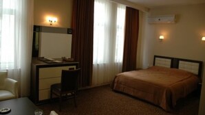 A hotel room with a bed, a desk with a chair, a small table, and a mirror. - Grand Adanus Hotel (Adana)
