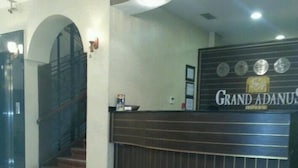 A reception area with a dark wood reception desk, a leather chair, and a staircase leading to an upper floor. - Grand Adanus Hotel (Adana)