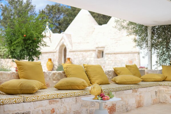 A stone bench with yellow cushions and a small table with flowers.