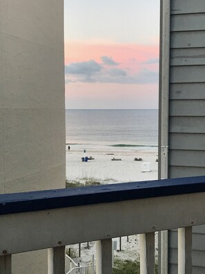 A view of a beach from a balcony with a railing, a clear sky, and the ocean in the background.