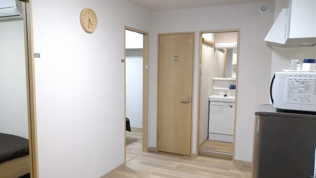 A hotel room with a bed, a wooden floor, a bathroom with a sink and mirror, and a microwave on a cabinet. - Issyuku Higashiueno Hotel 401 (Taito City)