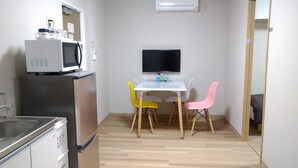 A compact kitchen with a microwave, refrigerator, and sink. There is a small dining area with a white table and colorful chairs. A flat-screen TV is mounted on the wall above the table. - Issyuku Higashiueno Hotel 401 (Taito City)