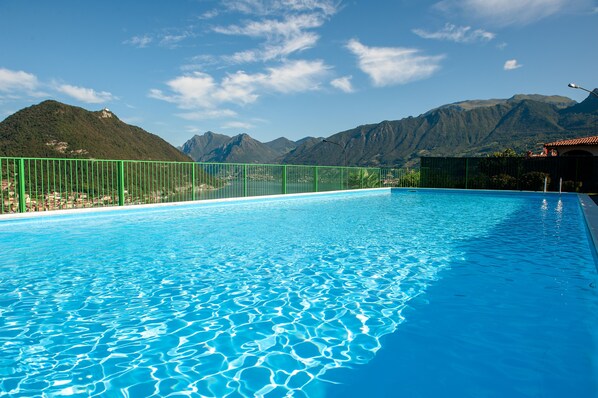 Une piscine entourée d’une clôture verte, avec des montagnes en arrière-plan.