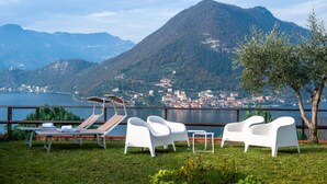 Eine Terrasse mit weißen Lounge-Stühlen und einem Tisch mit Blick auf einen See und Berge.
