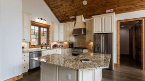A spacious kitchen with white cabinetry, a granite island, stainless steel appliances, and a wooden ceiling. - Clouds Rest- luxury pet friendly home in Eagles Nest with hot tub, year round views, and more (Banner Elk)