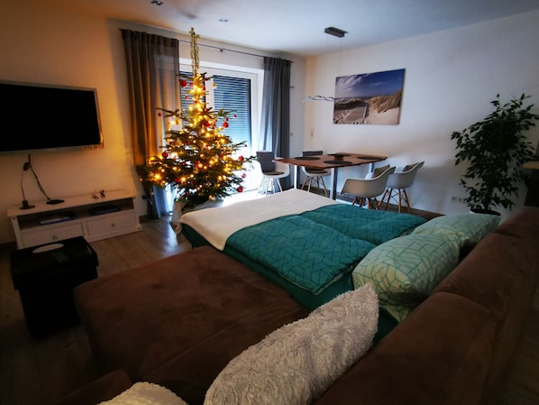A hotel room with a bed, a brown sofa, a Christmas tree, a TV, a desk, and a chair.