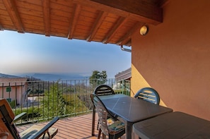 Un balcon avec une table et des chaises, donnant sur un paysage pittoresque avec des bâtiments et des arbres.