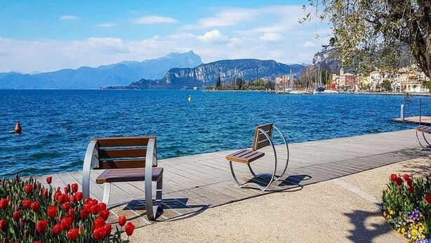A waterfront promenade with benches, a clear view of the sea, and a distant mountain range. - Dimora Miralago -  with panoramic view of the lake (San Zeno Di Montagna)