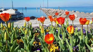 A coastal scene with a stone pier, tulips, and a boat docked near the water. - Dimora Miralago -  with panoramic view of the lake (San Zeno Di Montagna)