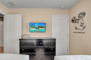 Une chambre à coucher avec un lit, une commode, un téléviseur fixé au mur et un autocollant mural représentant Mickey Mouse.