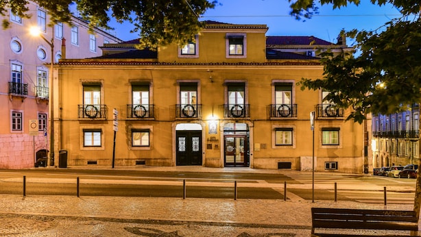 A building with a symmetrical facade, multiple windows, and a central entrance with a door and a small balcony. - Casa de Sao Mamede Hotel (Lisbon)