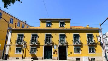 Edifici groc amb moltes finestres i balcons, una porta verda i un cartell que indica un restaurant.