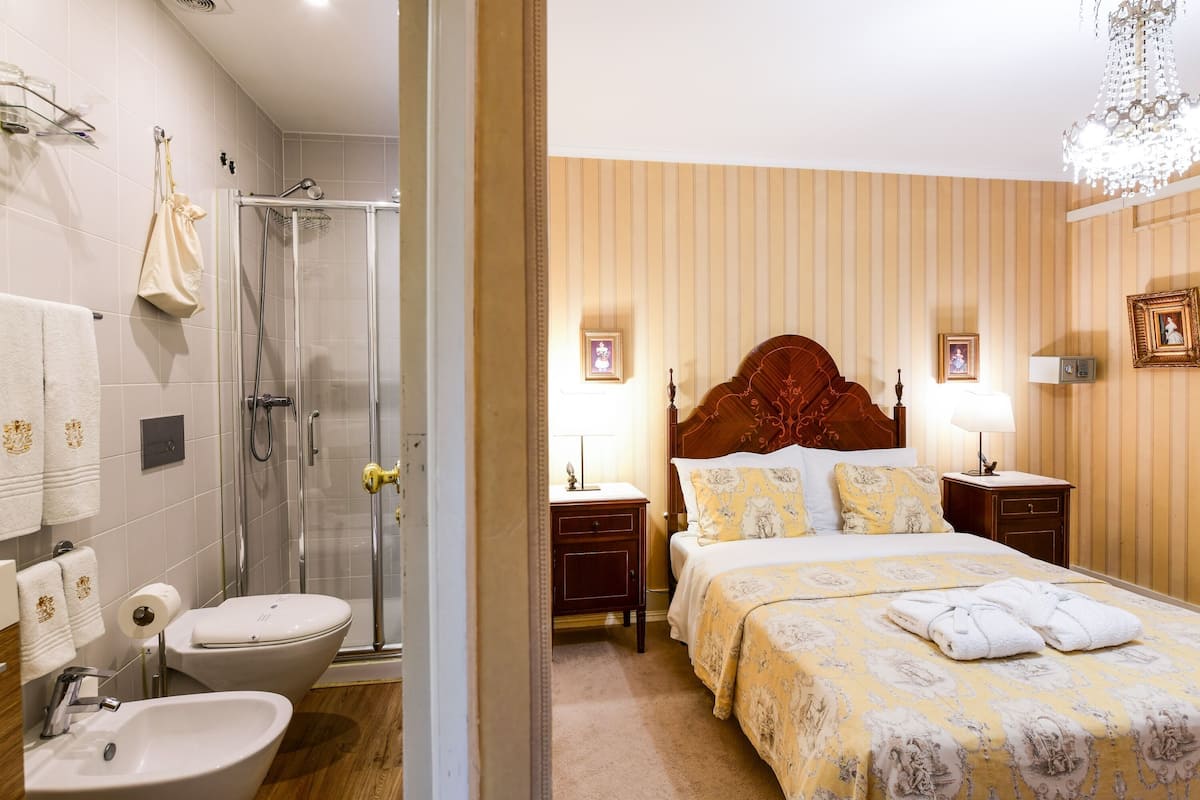 A hotel room with a shower, toilet, sink, and a bed with a wooden headboard.