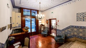 A lobby with a wooden reception desk, two armchairs, a chandelier, and patterned tile walls. - Casa de Sao Mamede Hotel (Lisbon)