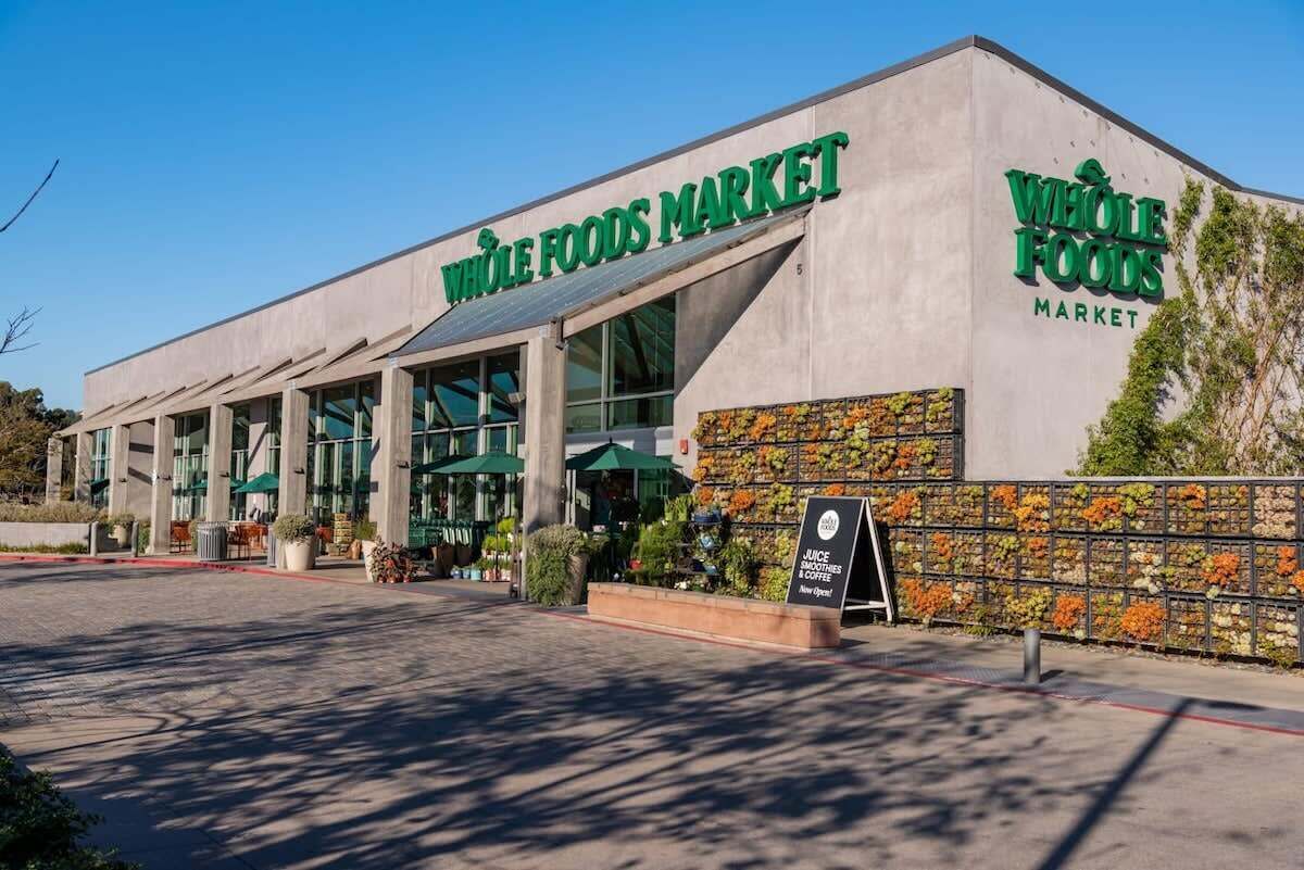 A Whole Foods Market with a modern facade, large windows, and a signboard advertising juice smoothies and coffee.