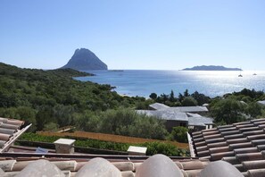 A coastal view with a prominent mountain, a beach, and a sea with boats. - Aria di Vacanza - Costa Dorata Cod 4 (Loiri Porto San Paolo)