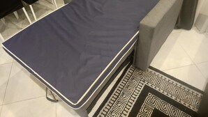A small, rectangular bed with a dark blue mattress and white trim, positioned between two gray armchairs in a room with tiled flooring. - Building part of the city's heritage (Joinville-le-Pont)