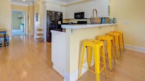 A kitchen with white cabinets, a black refrigerator, a microwave, and a yellow island with stools.