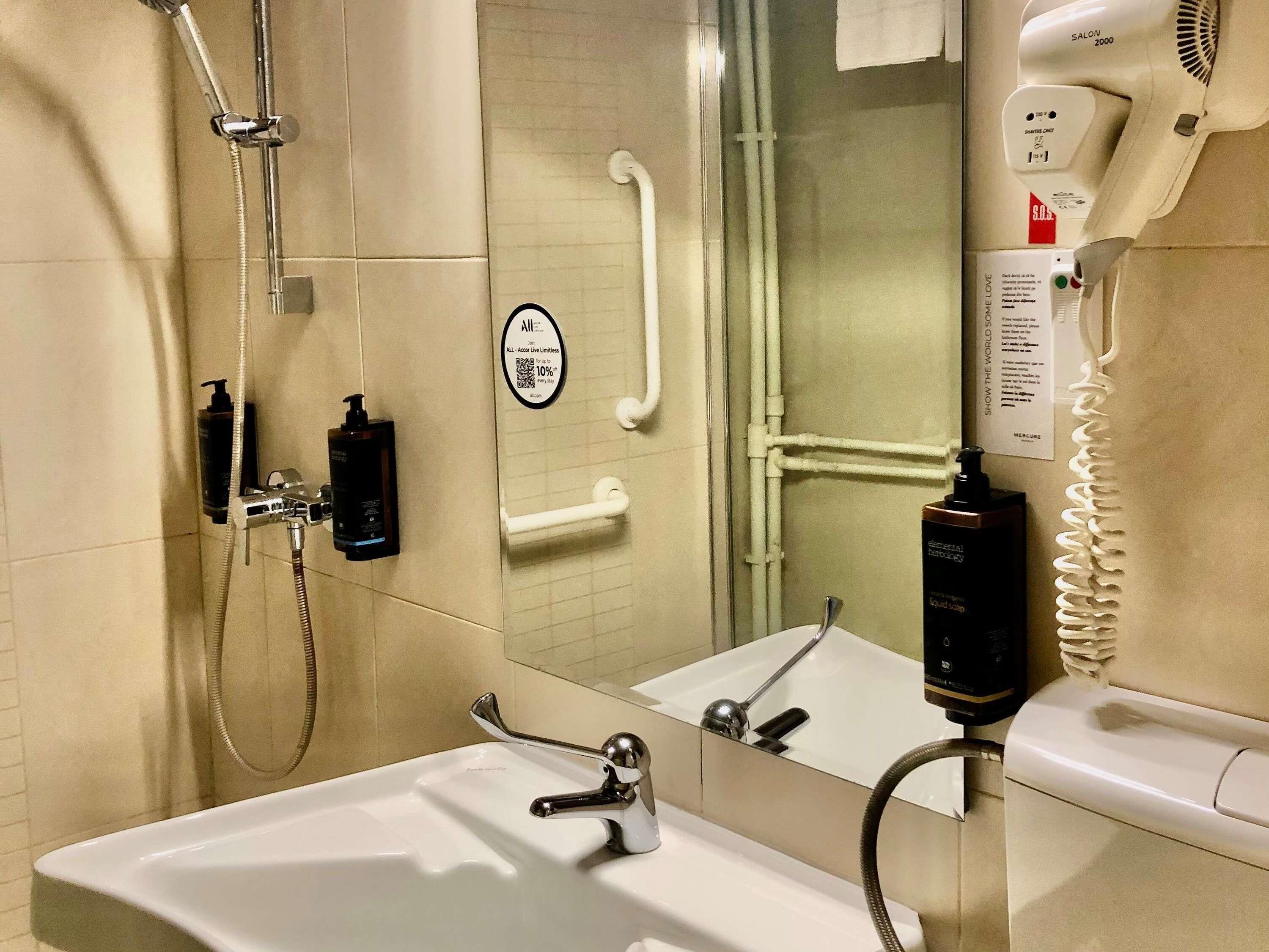 A bathroom with a shower, a sink, a mirror, and a hairdryer.