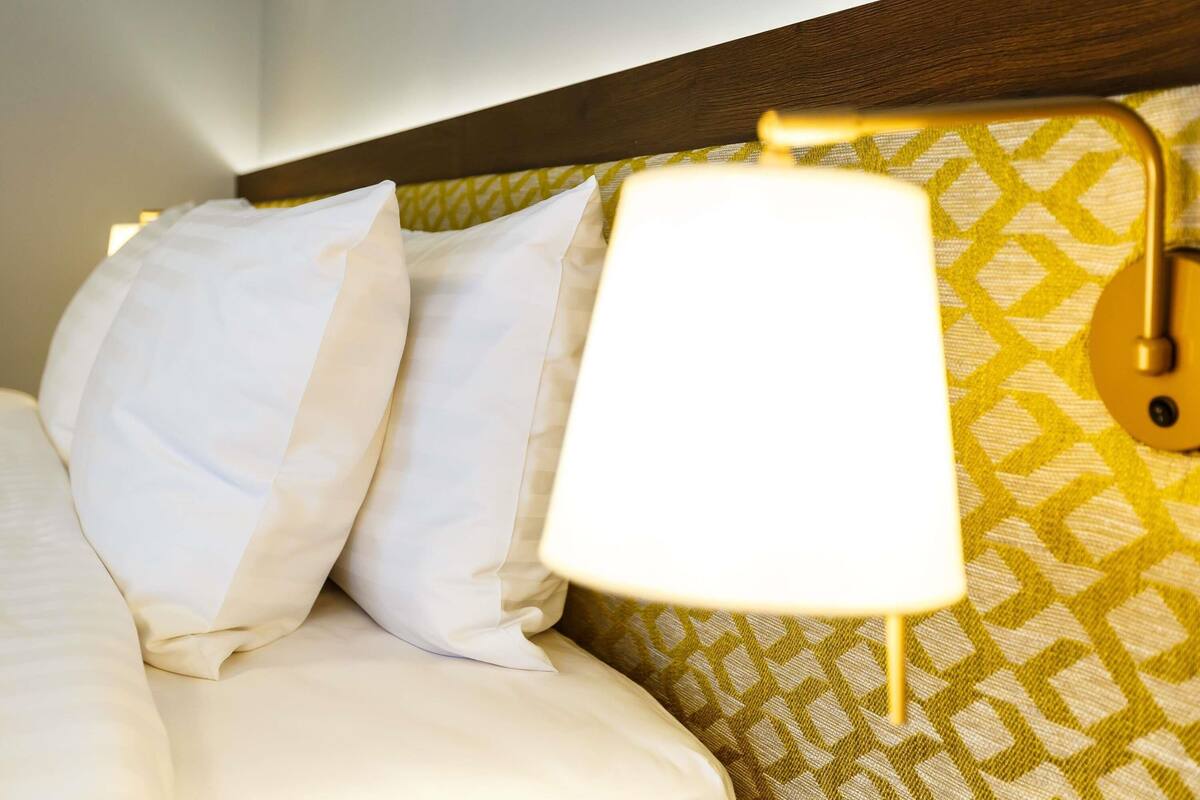 A bed with white linens and a patterned wall behind it.