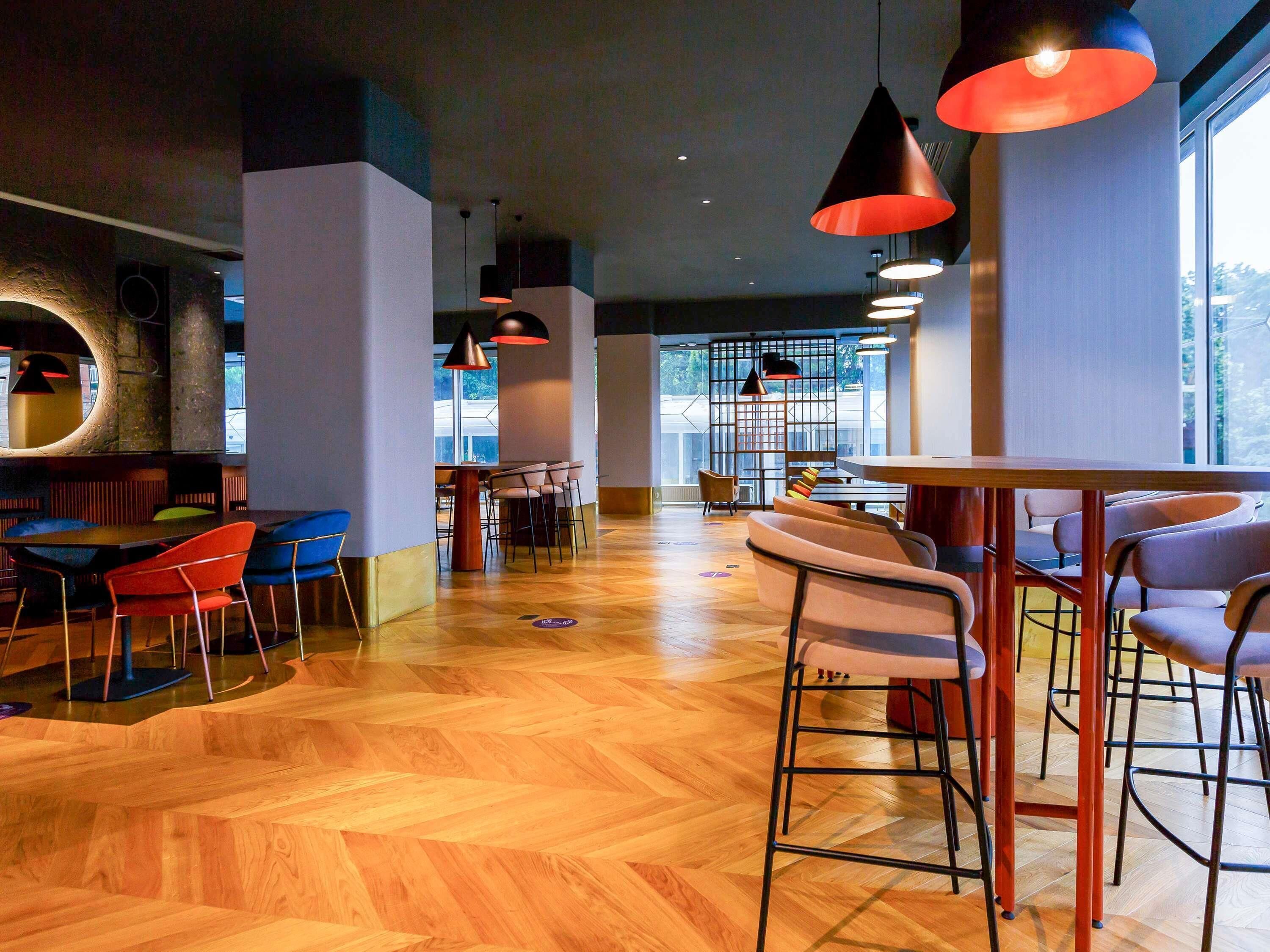 Un interior moderno con suelo de madera, asientos tipo barra e iluminación colgante.